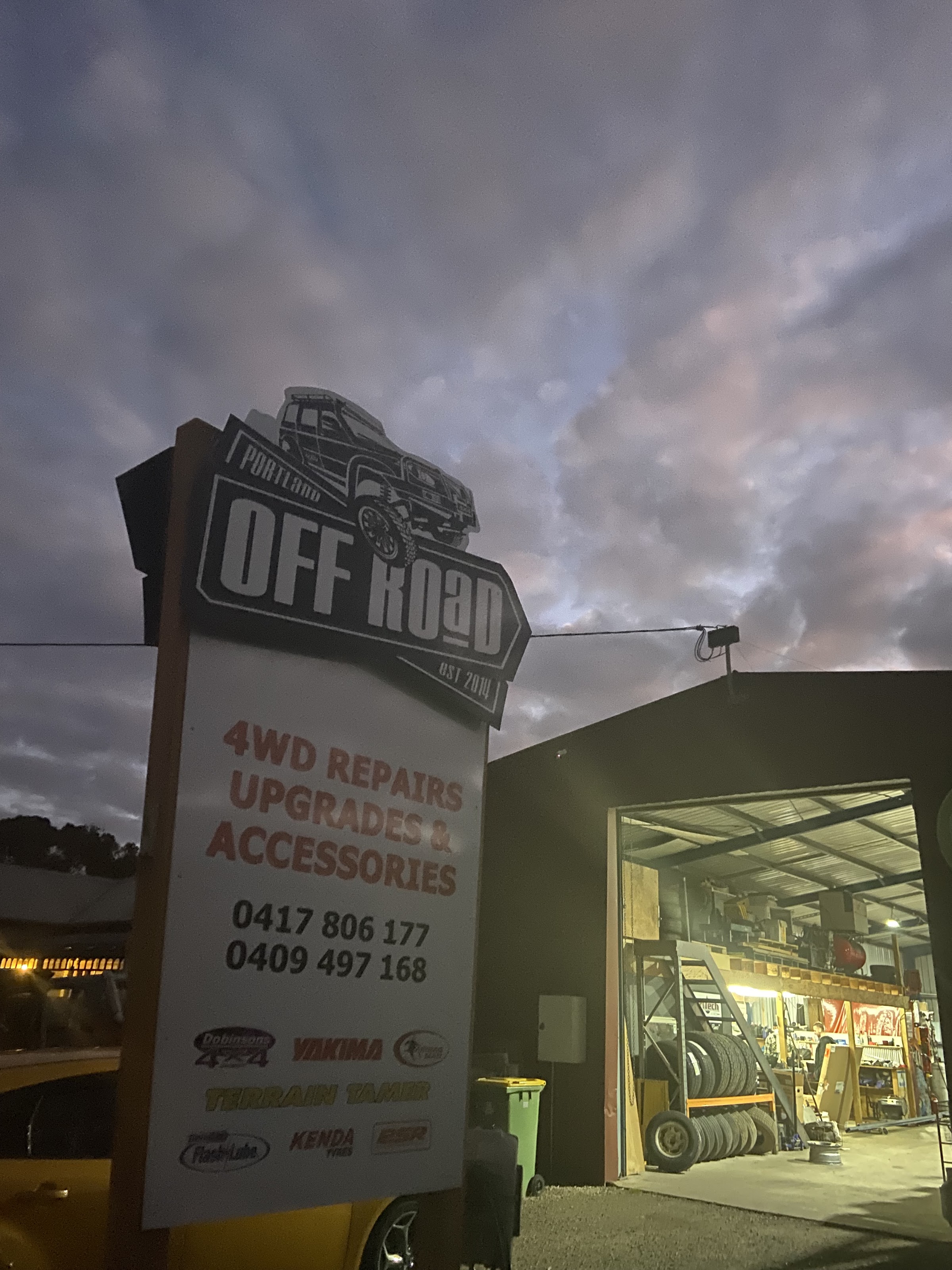 The Portland Off Road sign lit against the evening sky with the workshop open behind it