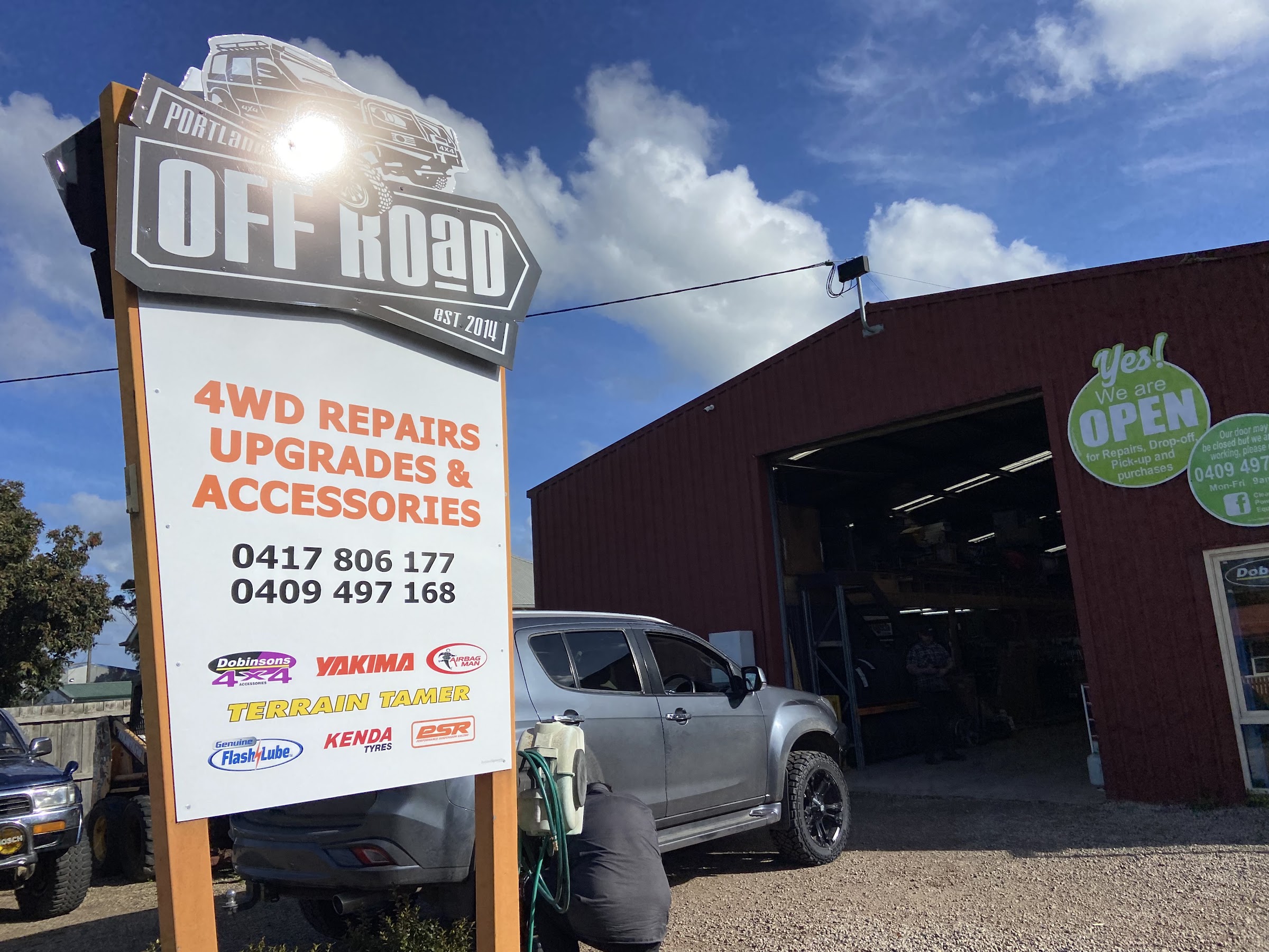 The Portland Off Road shopfront in daylight, sign at the kerb and the workshop roller door open