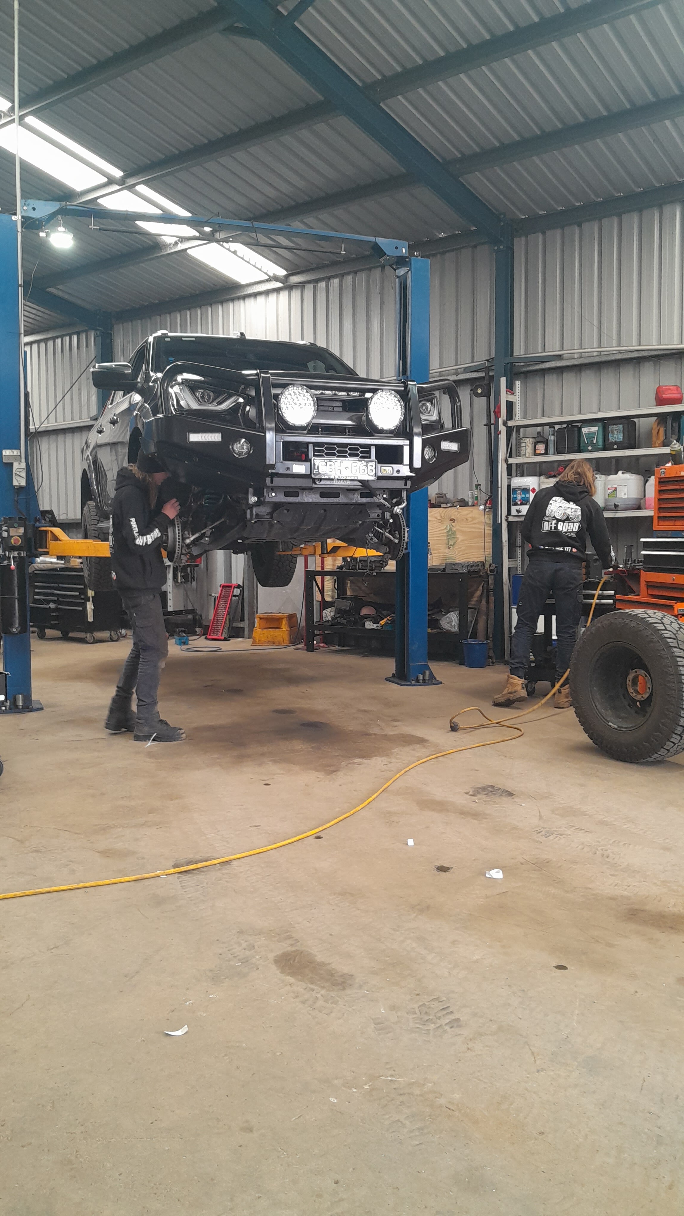 Two Portland Off Road staff working on a dual cab ute raised on the workshop hoist
